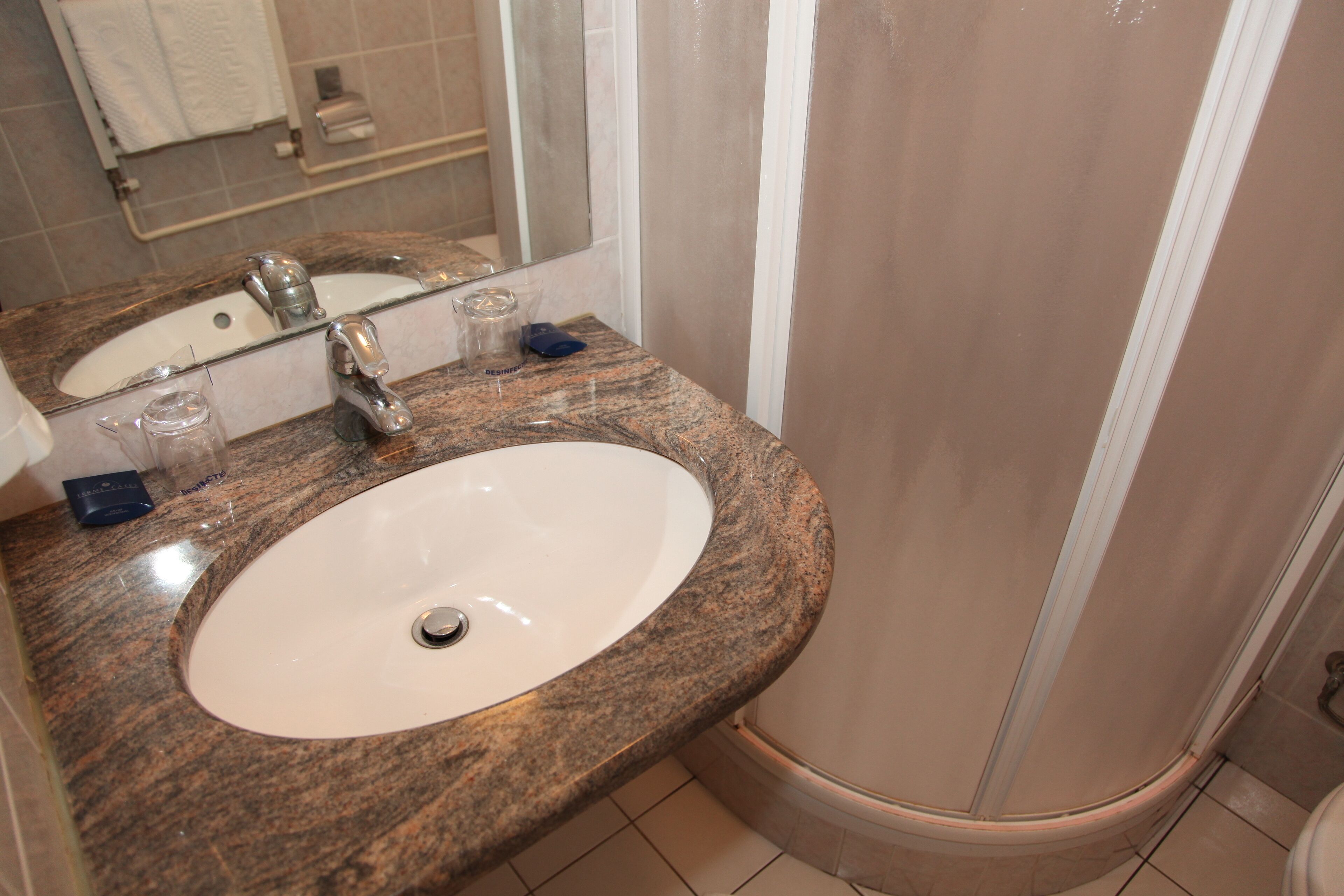 Un baño con encimera de granito, lavamanos blanco y cabina de ducha con mampara de vidrio.