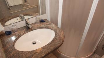 Un baño con encimera de granito, lavamanos blanco y cabina de ducha con mampara de vidrio.