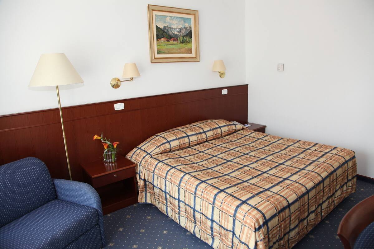 A hotel room with a bed, a nightstand, a lamp, a chair, and a painting on the wall.