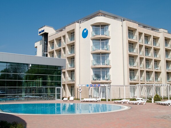 A hotel with a pool, multiple balconies, and a clear blue sky.