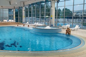 An indoor swimming pool with clear water, surrounded by large windows and sun loungers.