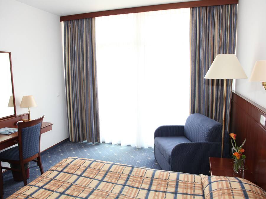 Une chambre d’hôtel comprenant un lit, un bureau avec une chaise, un canapé et deux lampes fixées au mur.