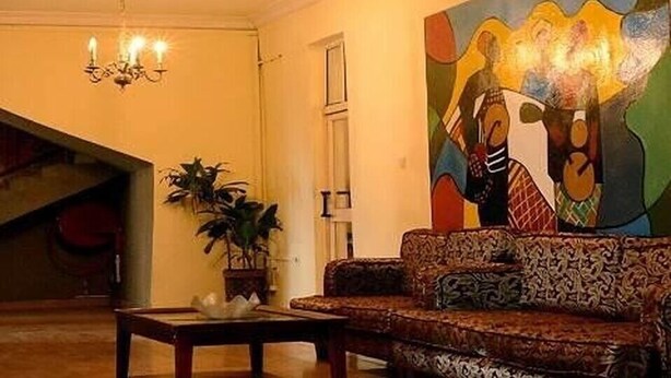 Uma sala de estar com um sofá estampado, um candelabro e um quadro abstrato colorido na parede.
