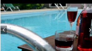 Ambiente à beira da piscina com um copo e uma garrafa de vinho tinto sobre uma mesa.