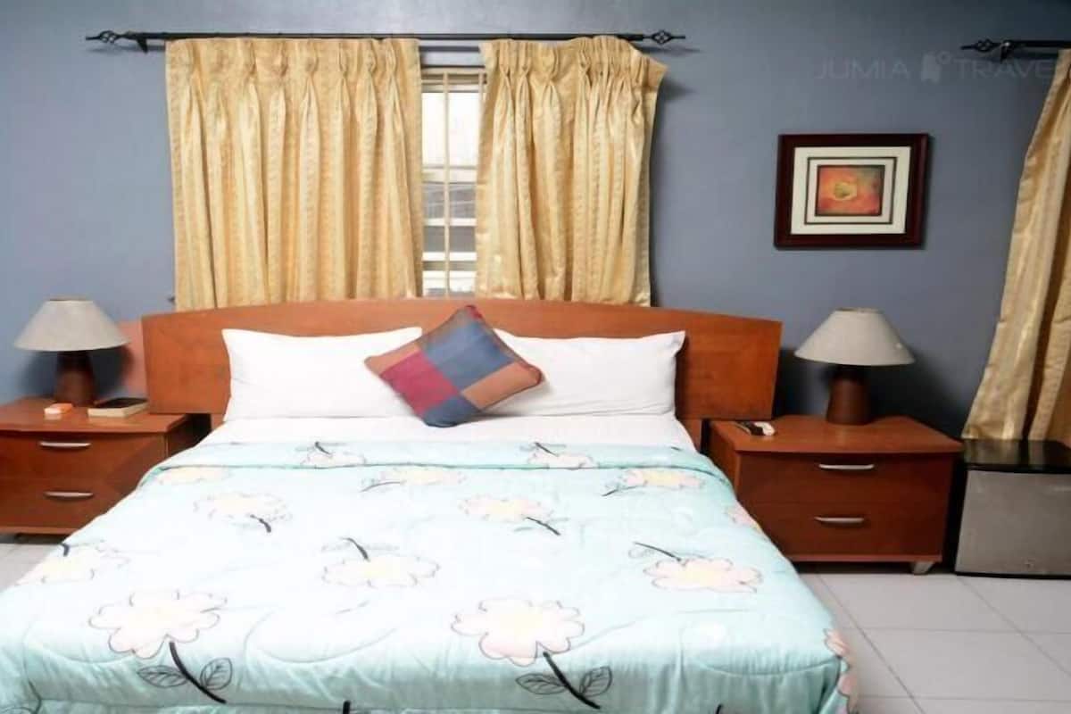 Une chambre à coucher comprenant un lit, deux tables de chevet, une commode, une fenêtre avec des rideaux et un tableau encadré accroché au mur.