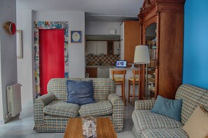 A living room with a checkered sofa, a red door, a kitchen in the background, and a lamp on a wooden side table. - PENTHOUSE WITH LARGE TERRACE IN CENTRAL CENTER OF CÁDIZ (Cádiz)