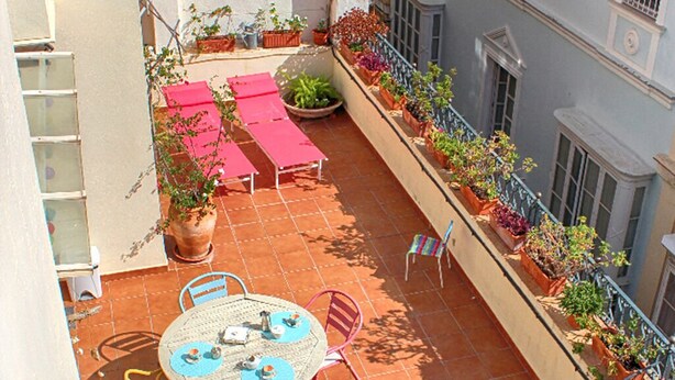 Terraço no telhado com mesa redonda, cadeiras, plantas em vasos e guarda-corpo.