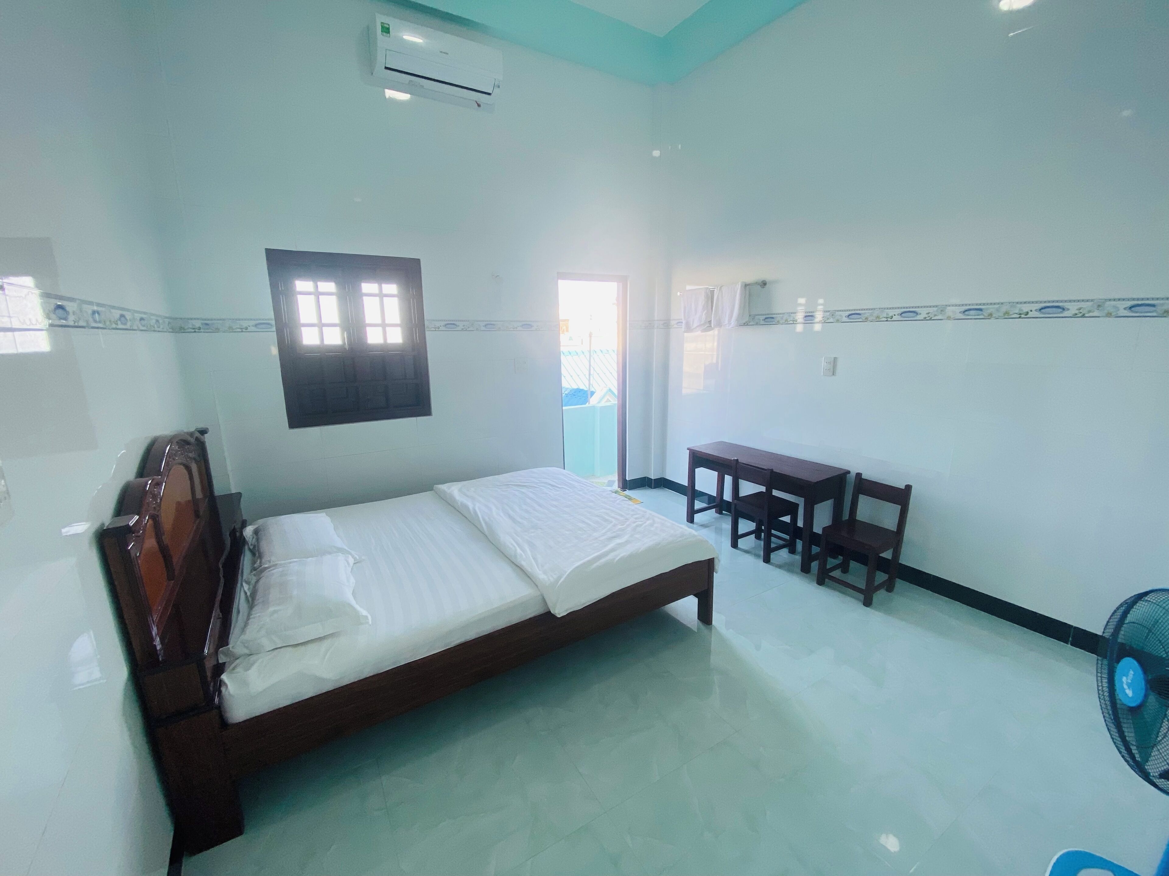 A room with a bed, a desk, and a fan.