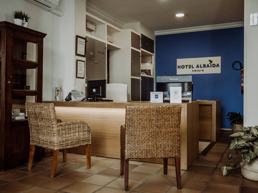 Zona de recepción de un hotel con un mostrador de madera, sillas de mimbre y una pared azul con un cartel que dice "HOTEL ALBAIDA nature".
