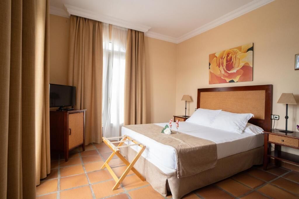 A hotel room with a bed, a television, a desk, and a painting on the wall.