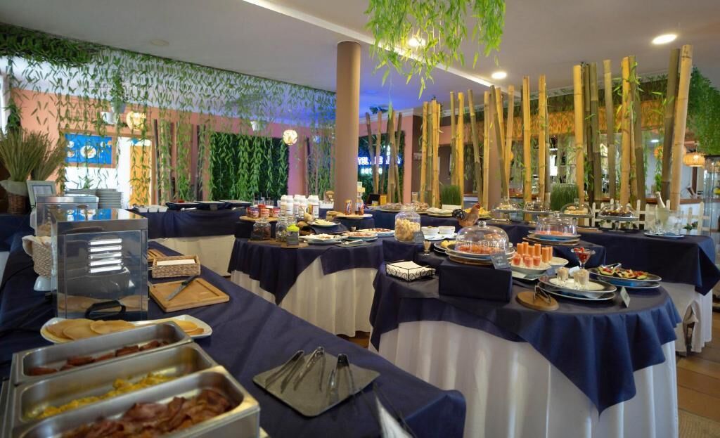 A buffet setup with various food items and utensils on tables, surrounded by decorative bamboo elements and indoor plants.