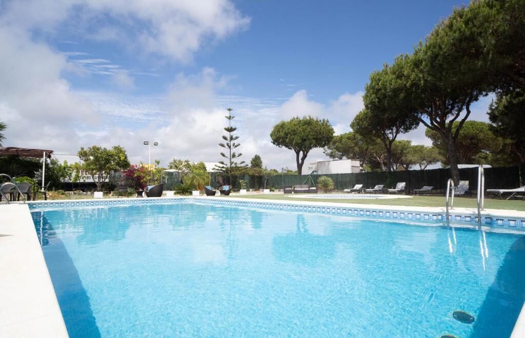 A swimming pool with a clear blue sky, surrounded by trees and lounge chairs.