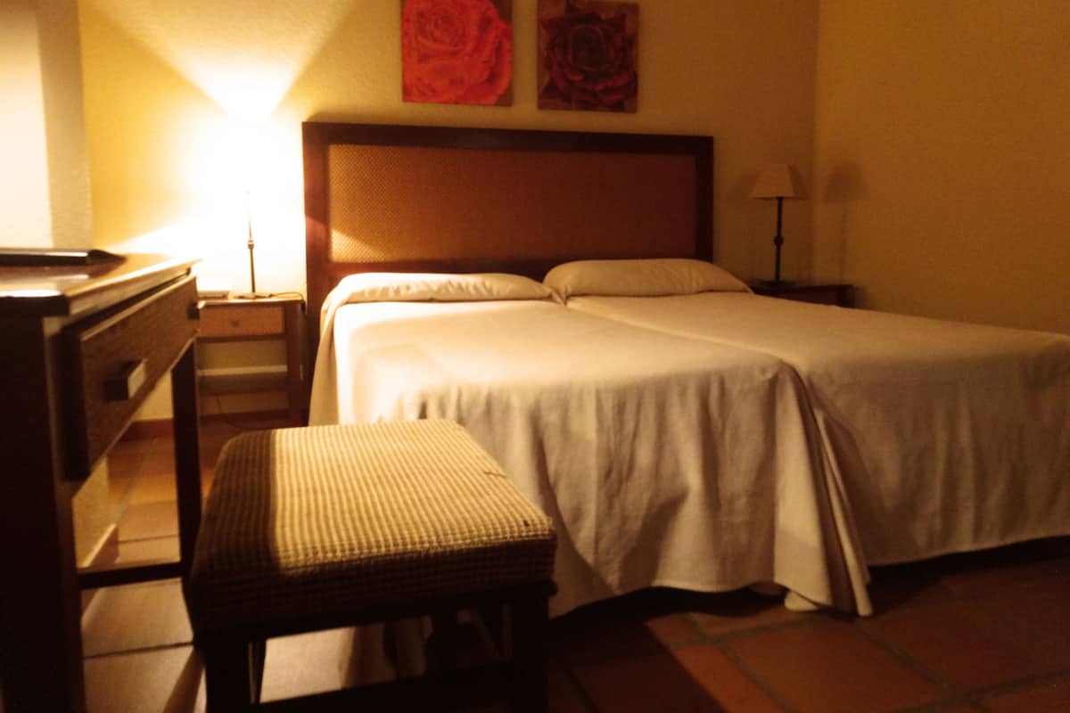 A hotel room with a bed, a desk, a chair, and two wall-mounted lamps.