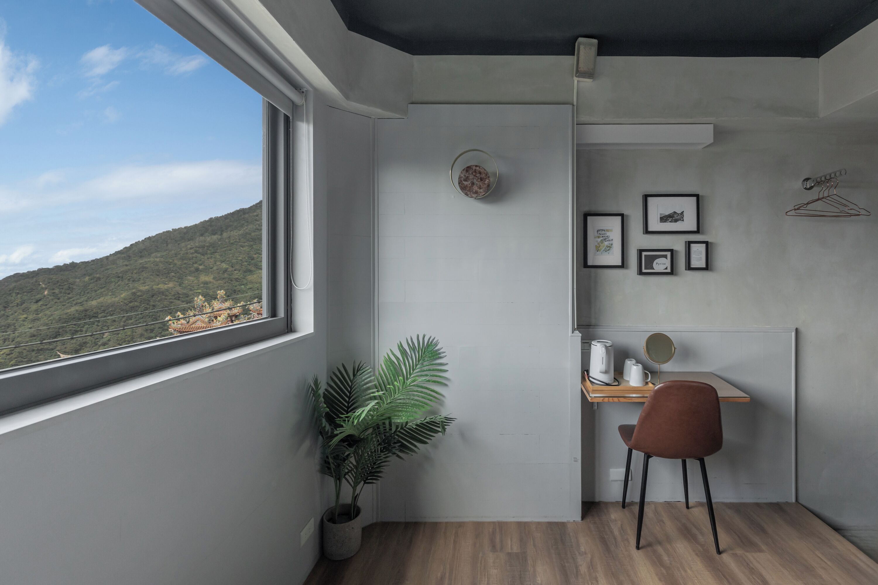 Habitación de esquina con vistas a la montaña, una planta en maceta, un escritorio con una silla y cuadros en la pared.