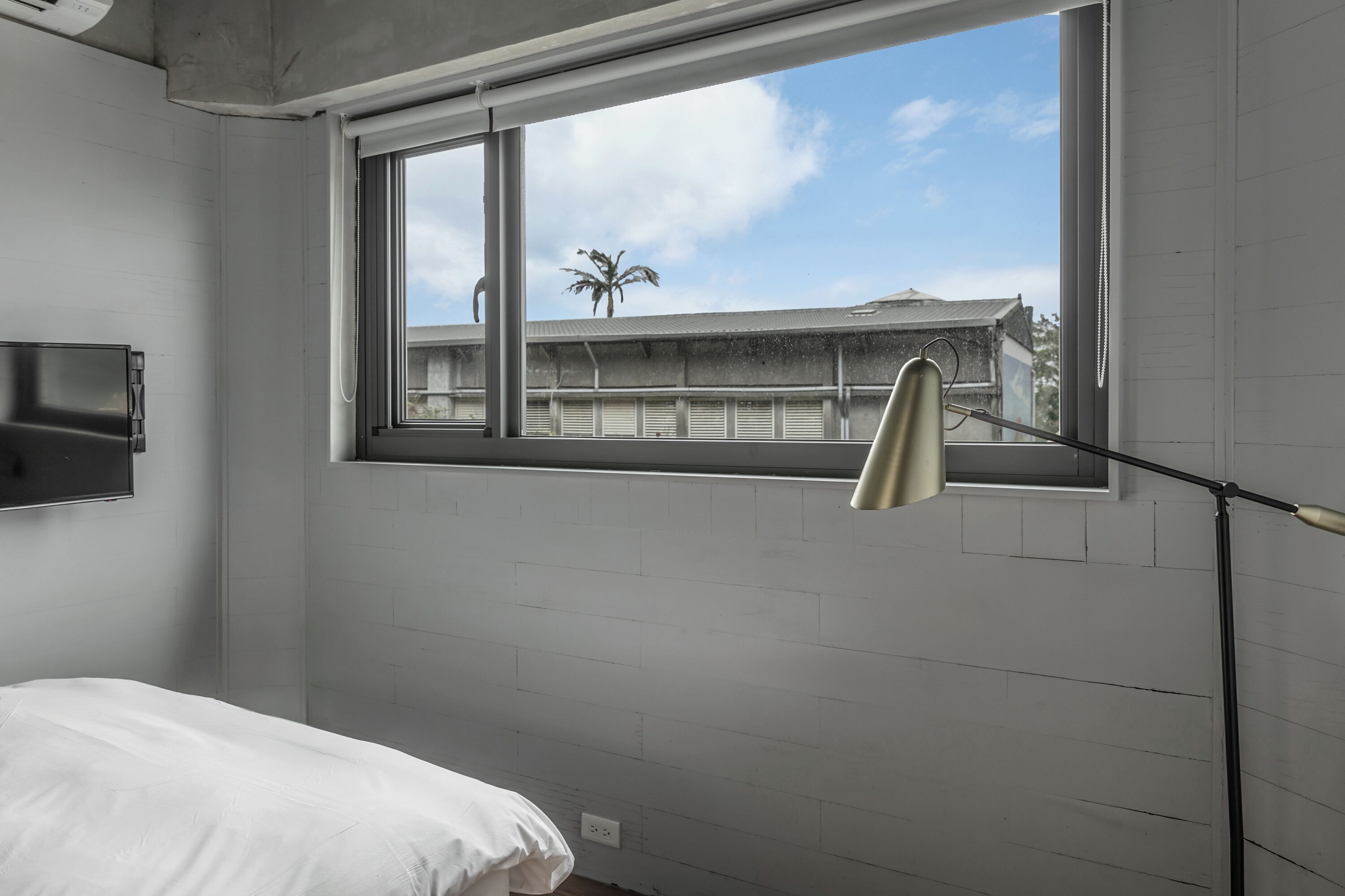 Een slaapkamer met een groot raam, een bed en een bureaulamp.