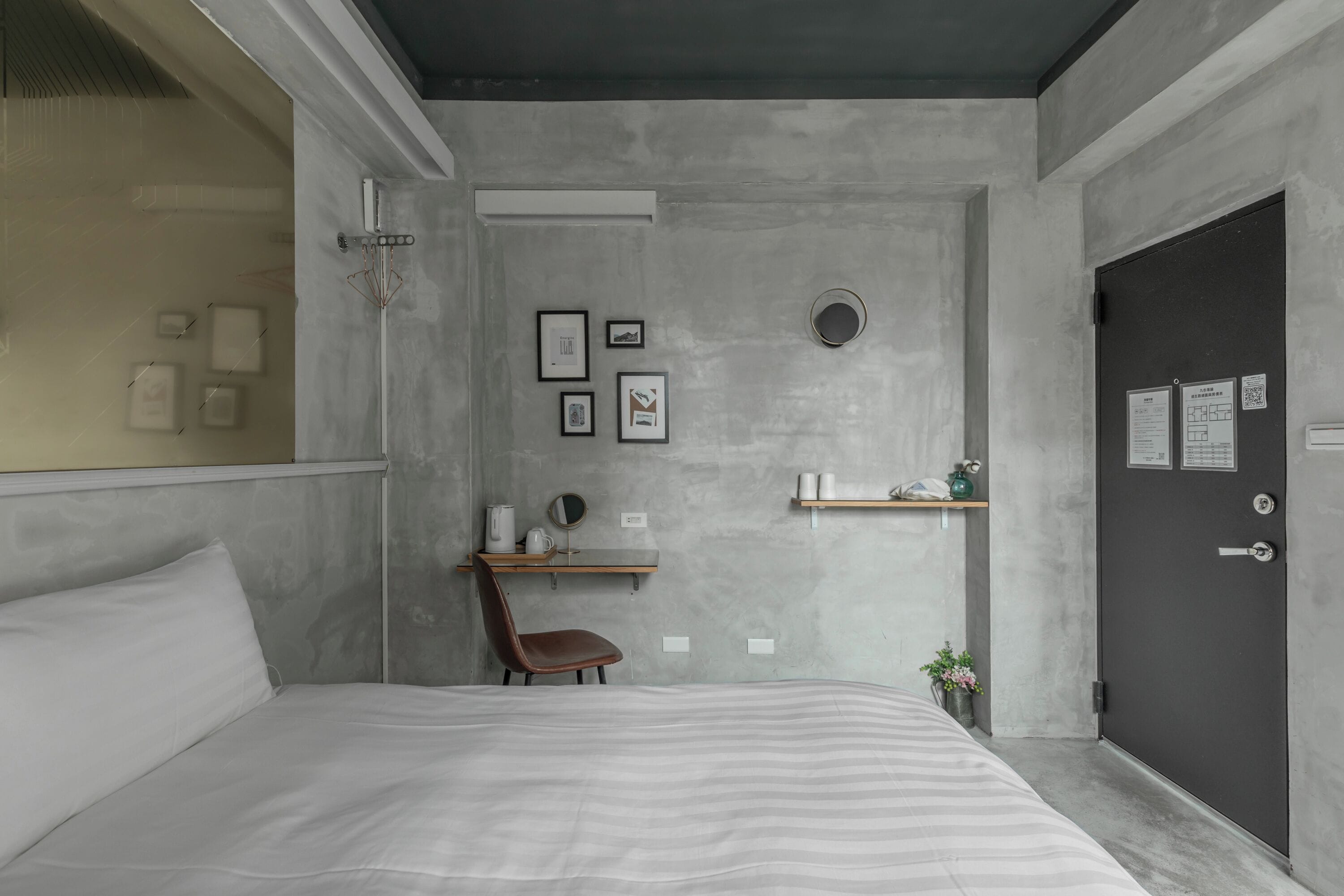 A modern bedroom with a bed, a desk, a chair, and a door.