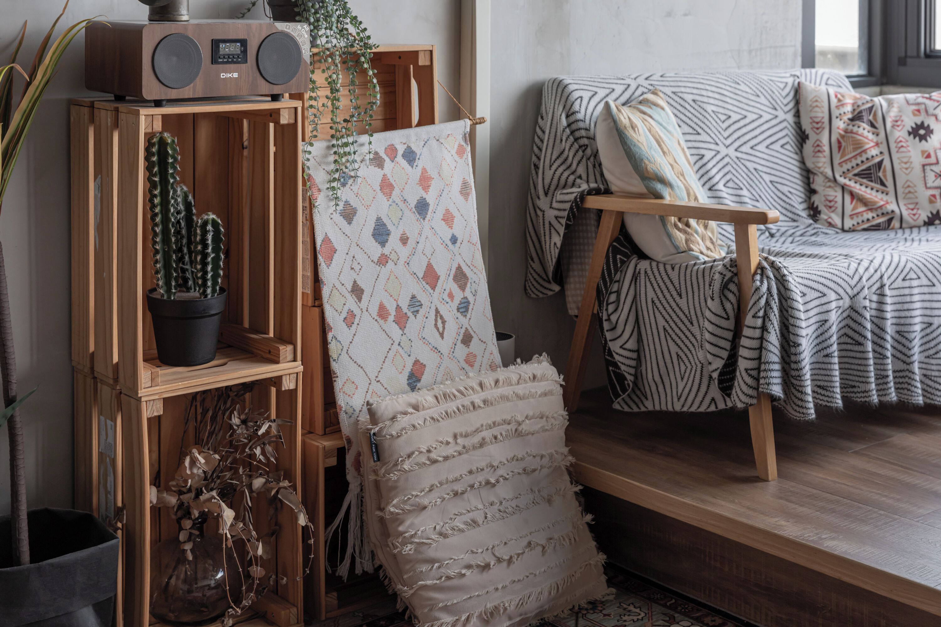 A cozy living room with a wooden bookshelf, a patterned throw pillow, and a cactus plant.