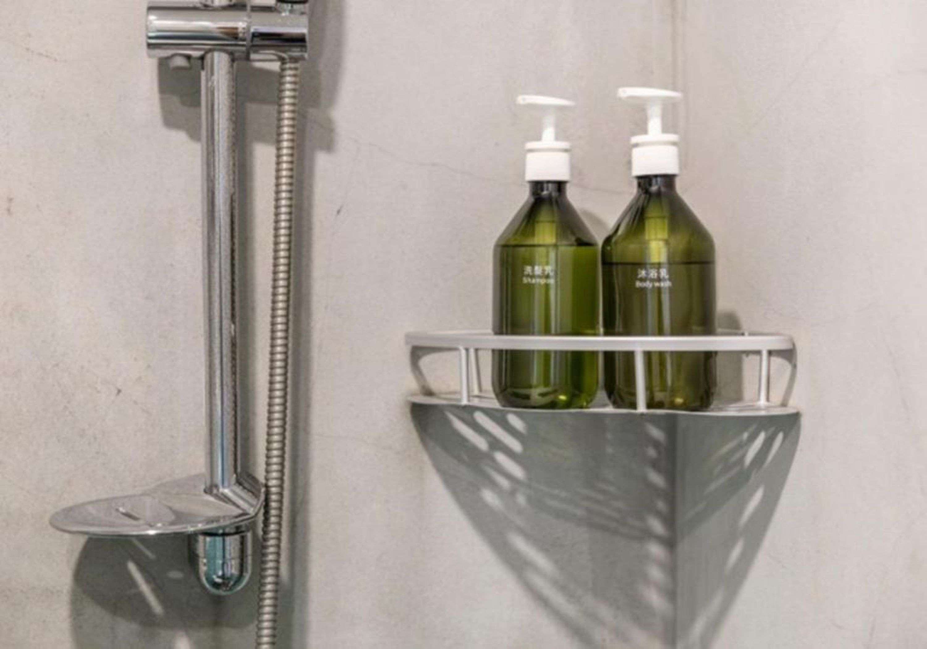 A shower area with a chrome hose and a shelf holding two bottles of shampoo.