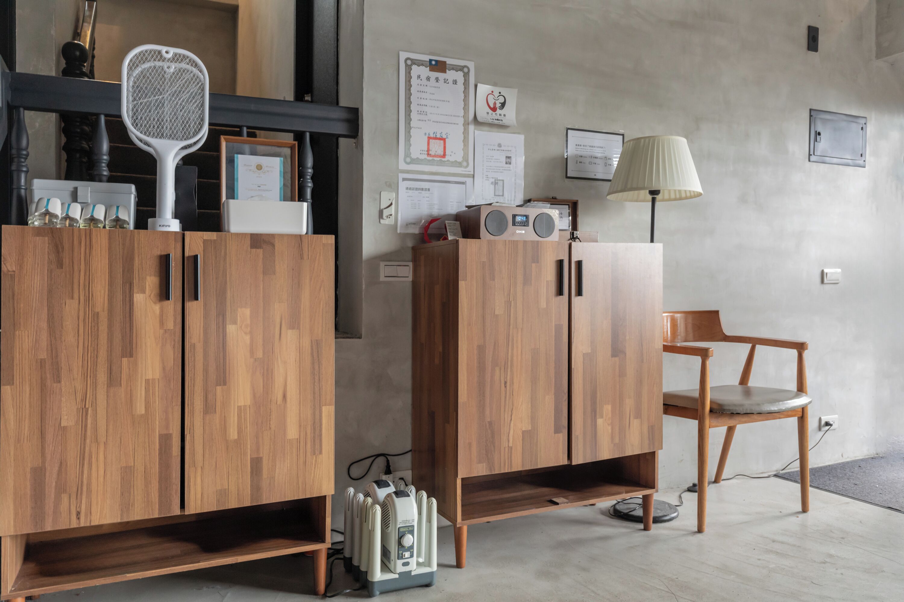 A room with wooden cabinets, a chair, a desk, and various items on the wall, including certificates and a lamp.