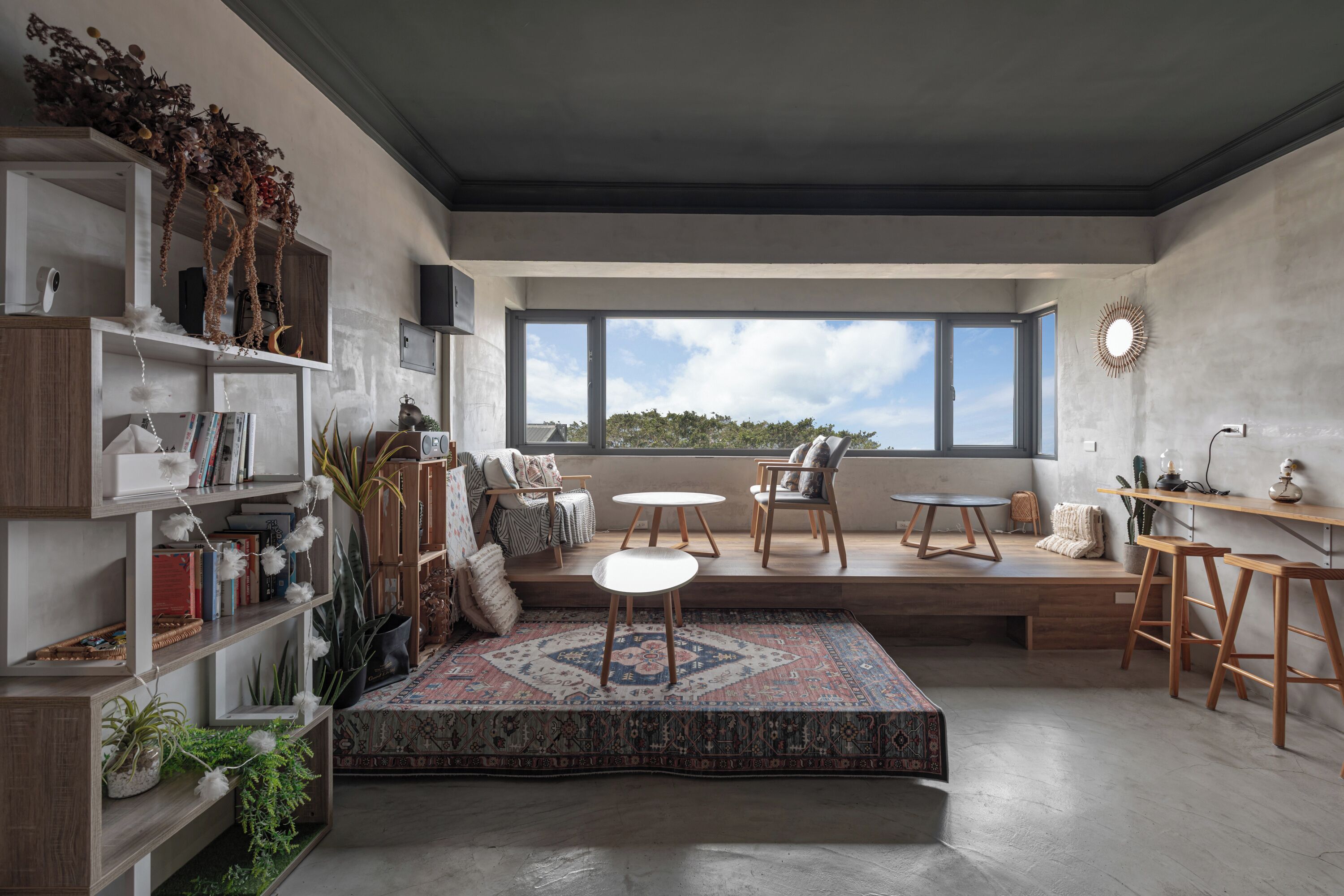 Una sala de estar moderna con un ventanal grande, estanterías empotradas, un tapete estampado y muebles de madera.