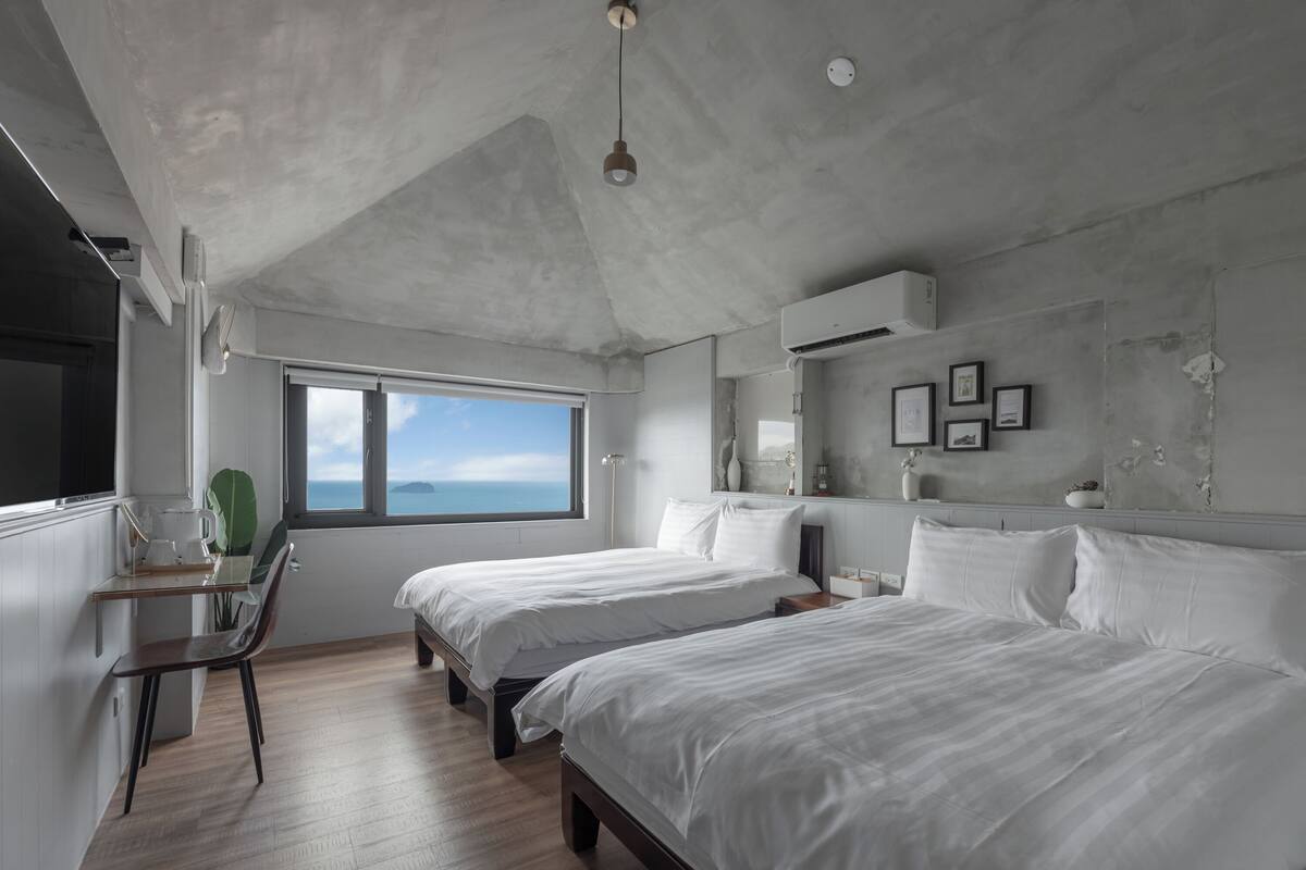 Un dormitorio moderno con dos camas, un escritorio y un ventanal con vistas al cielo.