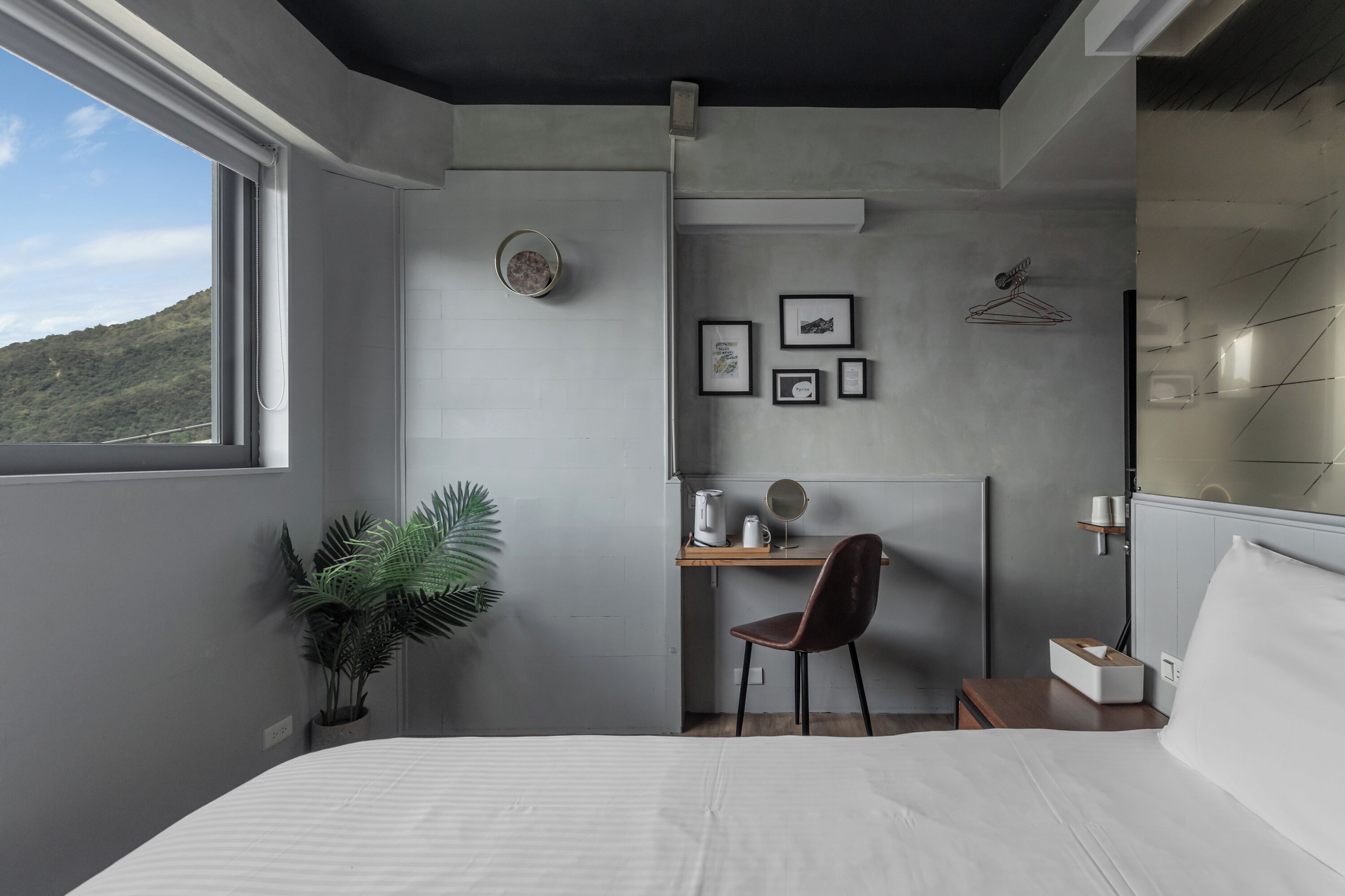 A modern bedroom with a bed, a desk, a chair, a potted plant, and a view of a mountain.
