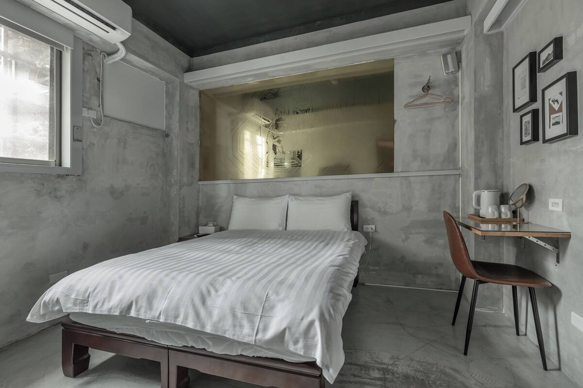Un dormitorio con una cama, una silla, un escritorio y un ventanal grande.