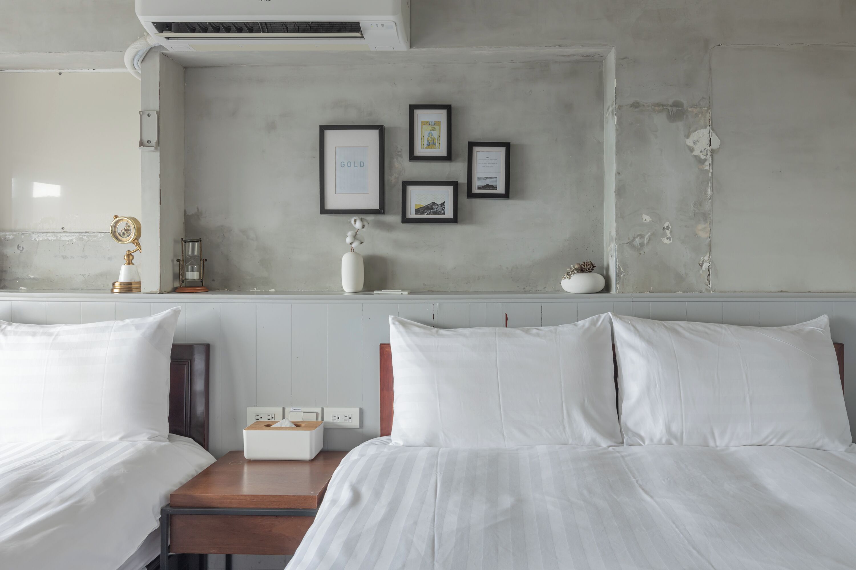 A hotel room with two beds, a small table, a nightstand, and a wall with framed pictures.