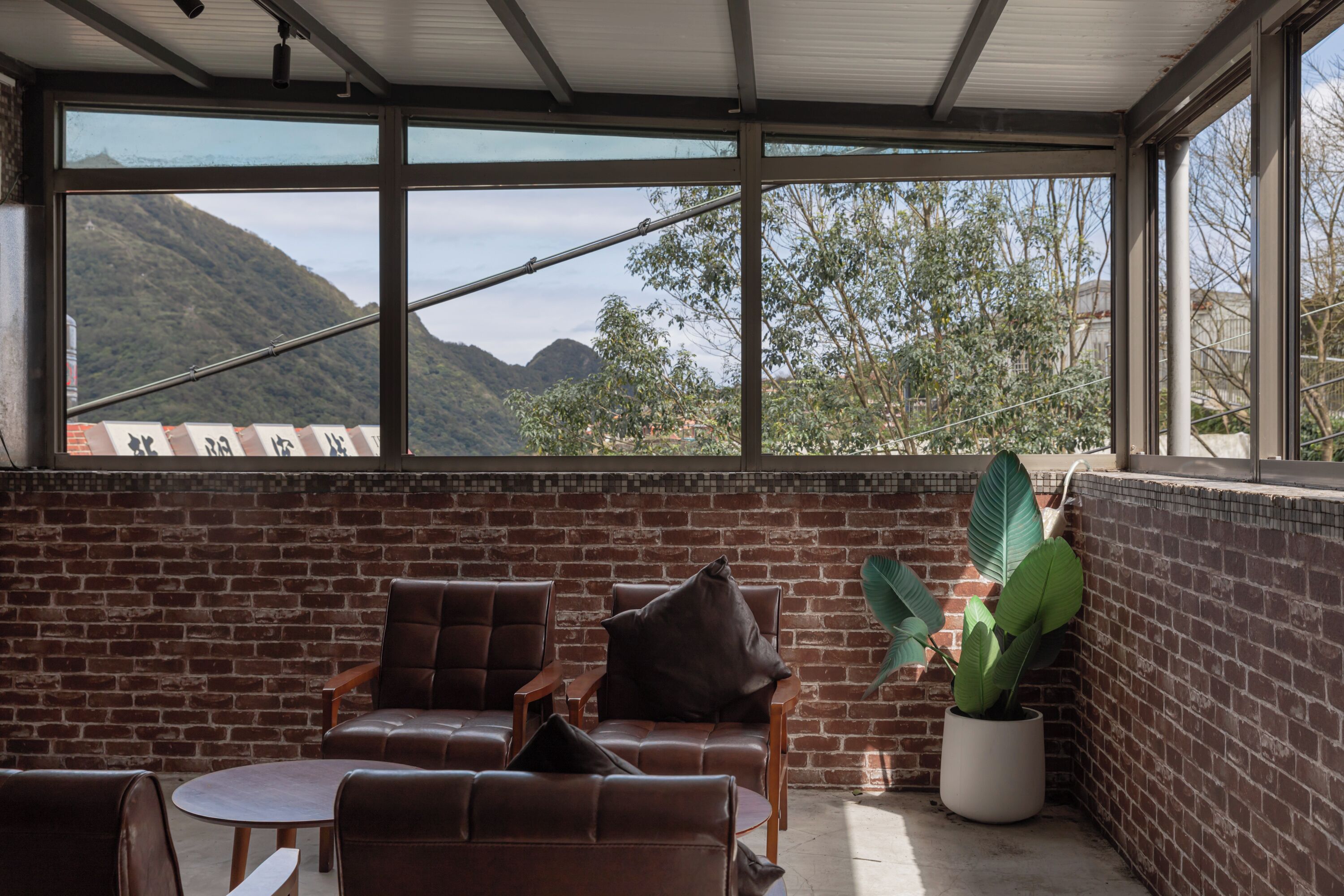 A sunlit room with brick walls, large windows, and leather chairs.