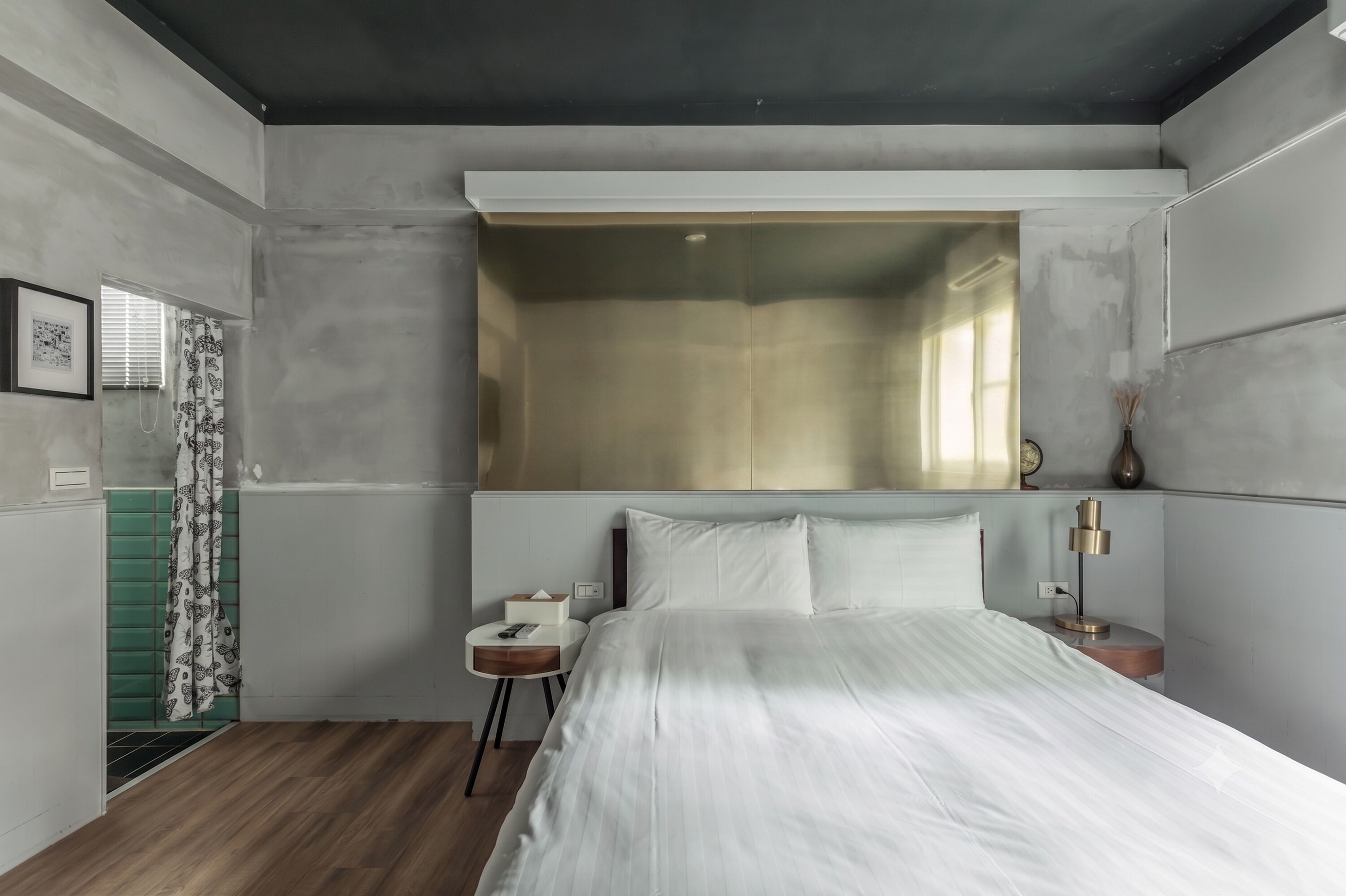 A bedroom with a large bed, a bedside table with a lamp, a green wall unit, and a window with curtains.