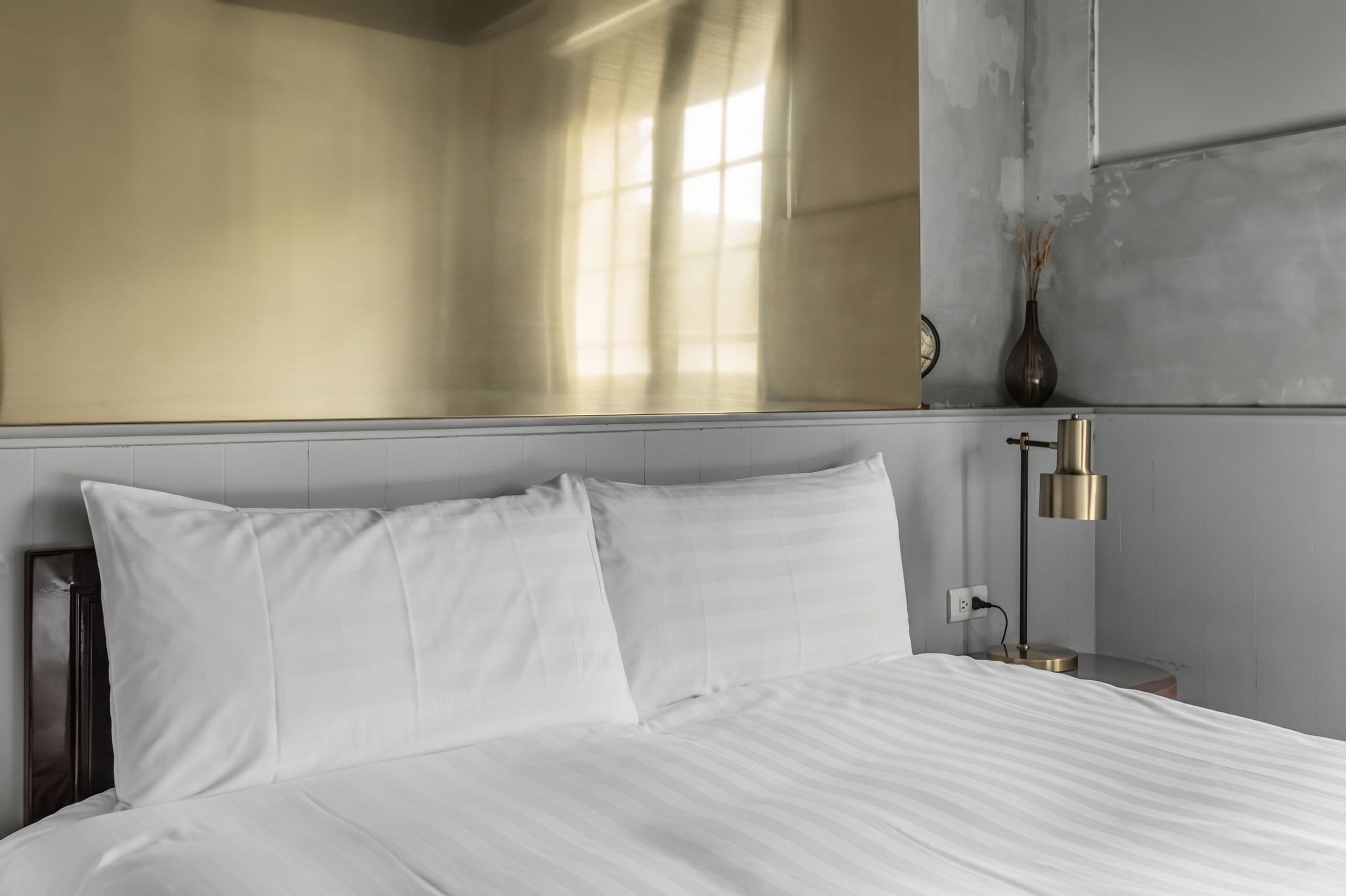 A neatly made bed with white linens, a bedside lamp, and a vase on the nightstand.