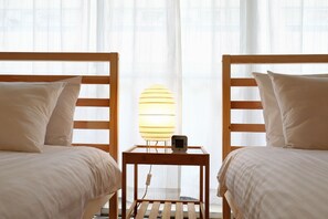 A hotel room with two wooden beds, a bedside table with a lamp, and sheer curtains. - Pebliss Kurenai No.2 (Tokyo)
