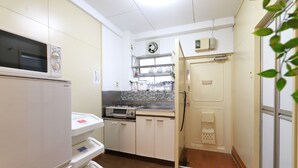 A compact kitchen with white cabinets, a microwave, a stove, and a sink. - Pebliss Kurenai No.2 (Tokyo)