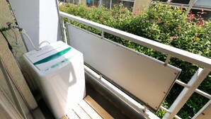 A balcony with a white metal railing, a white water dispenser, and a wooden bench. - Pebliss Kurenai No.2 (Tokyo)