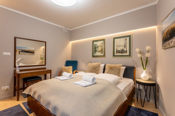 A neatly arranged bedroom with a large bed, bedside tables, a desk, and framed artwork on the walls.
