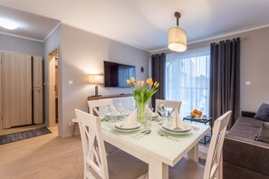 A dining area with a table set for four, a TV mounted on the wall, and a sofa in the background.