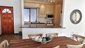 A dining area with a wooden table and chairs, a bowl of fruits, and a kitchen in the background. - Witsand 806 (Cape Town)