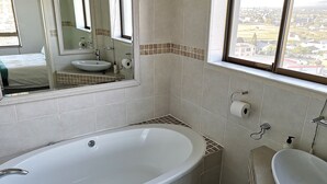 A bathroom with a bathtub, a sink, and a window offering a city view. - Witsand 806 (Cape Town)
