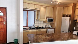 A kitchen with wooden cabinets, a microwave, a refrigerator, and a granite countertop. - Witsand 806 (Cape Town)