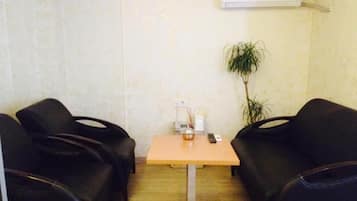 Een kleine kamer met twee zwarte leren stoelen, een houten tafel, een kleine plant in pot en een airconditioning op de muur.