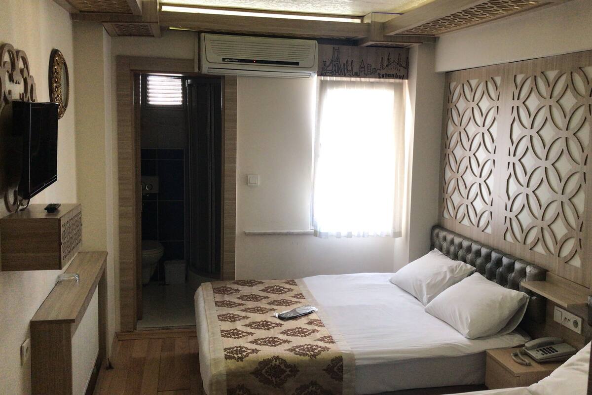 A hotel room with a bed, bedside table, and a wall-mounted TV.