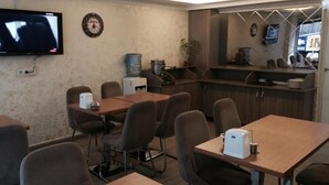 Uma sala de conferência com mesa de madeira, cadeiras, televisão, relógio e uma pequena copa.