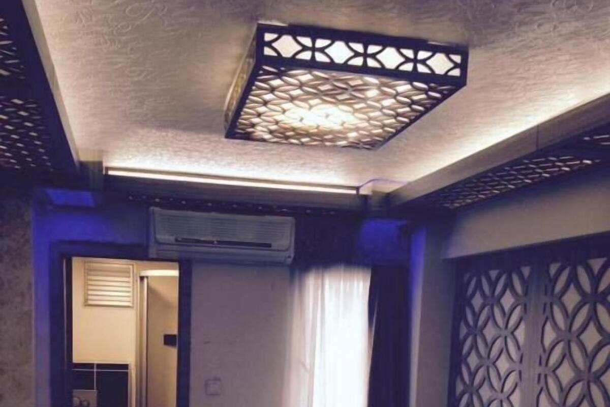 A hotel room with two beds, a bathroom with a toilet and shower, and a decorative ceiling light fixture.