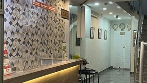 Uma área de recepção de hotel com parede estampada, balcão de recepção e escada que leva a um andar superior.