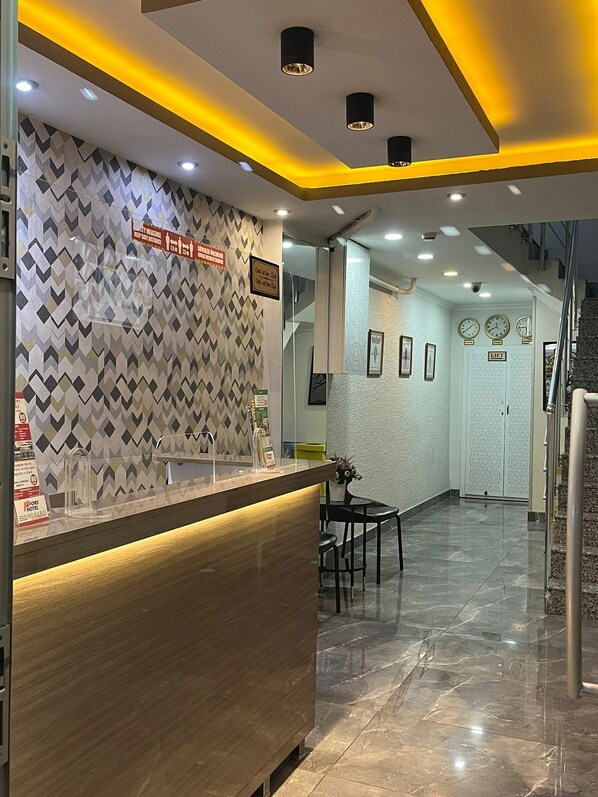 Zona de recepción de hotel con pared estampada, mostrador de recepción y una escalera que conduce a un piso superior.