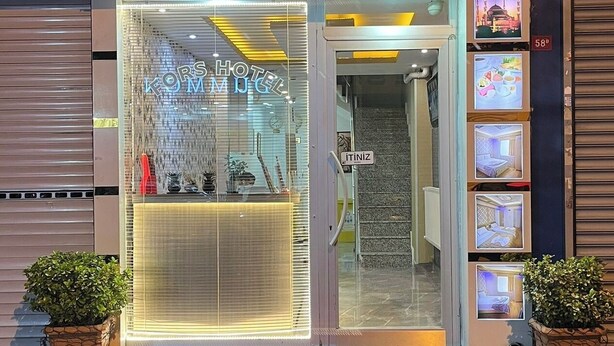 Entrada do Hotel Forsk com porta de vidro, tapete vermelho e plantas em vasos de ambos os lados.