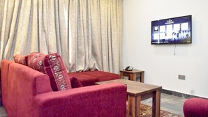 Een woonkamer met een rode bank, een houten salontafel en een aan de muur bevestigde televisie.
