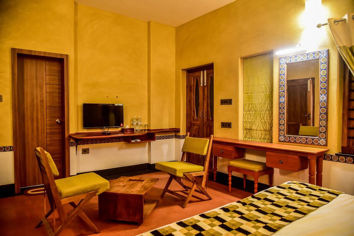Una habitación de hotel con un escritorio de madera, dos sillas, un televisor, una cama con colcha a cuadros y un espejo grande con marco decorativo.