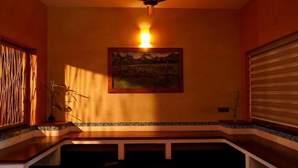 Une pièce dotée d’un ventilateur de plafond, d’un tableau représentant un paysage encadré, d’une plante en pot et d’une fenêtre avec des stores.