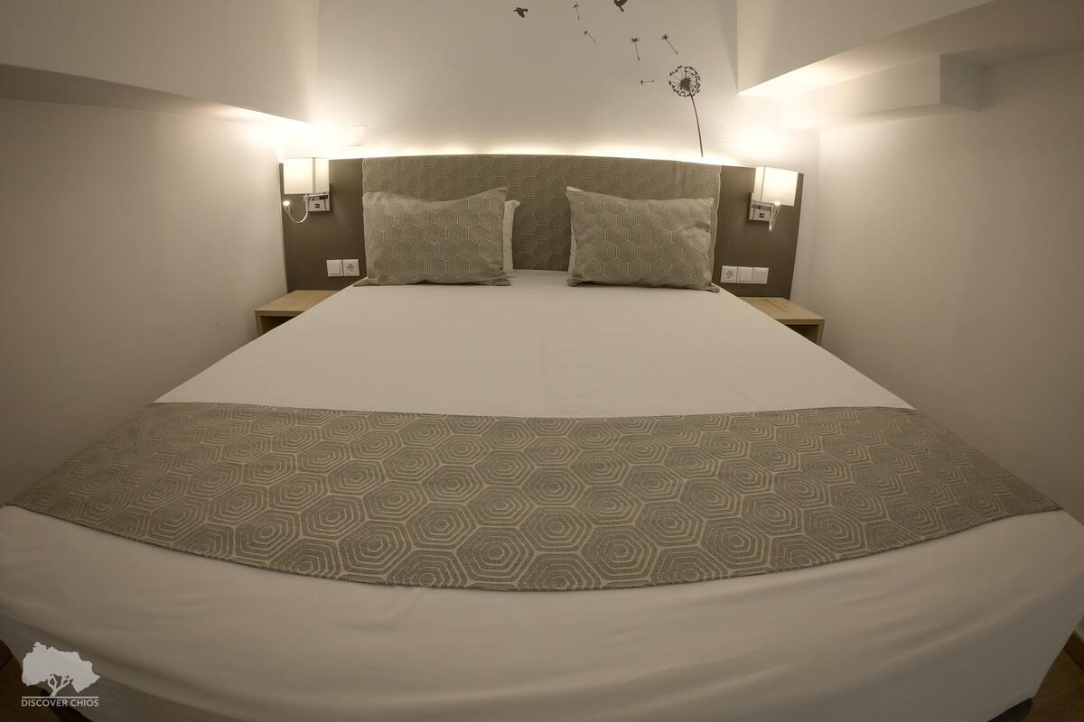 Una cama bien hecha con ropa de cama estampada, dos lámparas de pared y un adhesivo mural con pájaros y un diente de león.